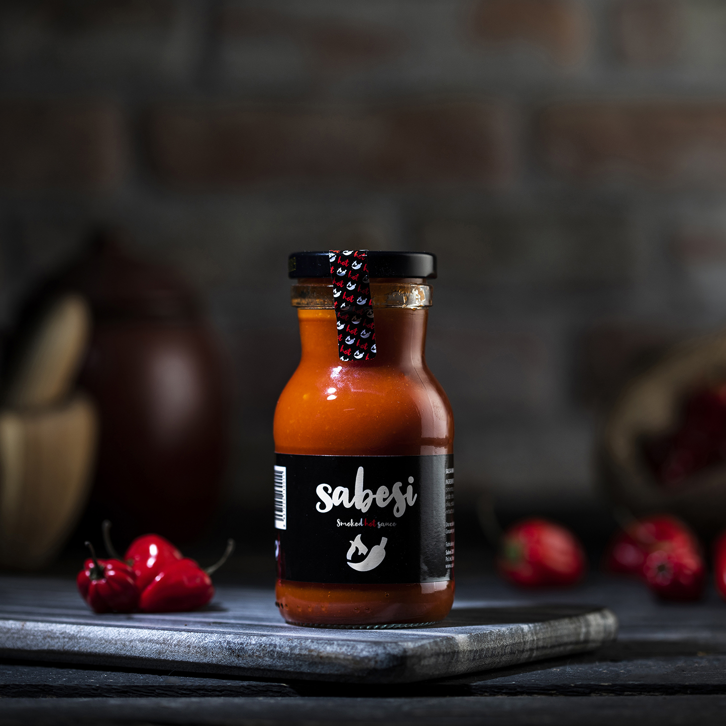 Botella de Sabesi Smoked Hot Sauce rodeada de ajíes habaneros