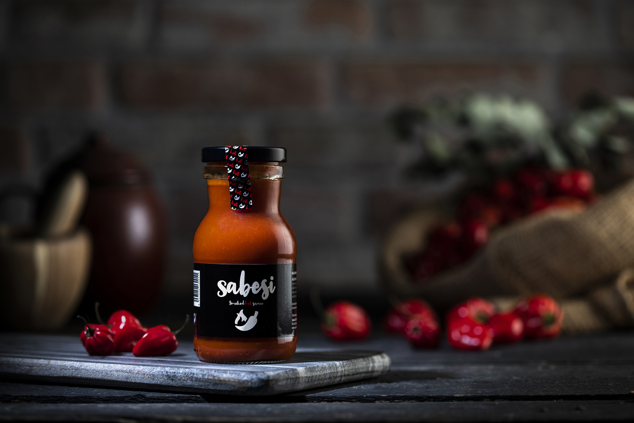 Botella de Sabesi Smoked Hot Sauce con ajíes habaneros al fondo